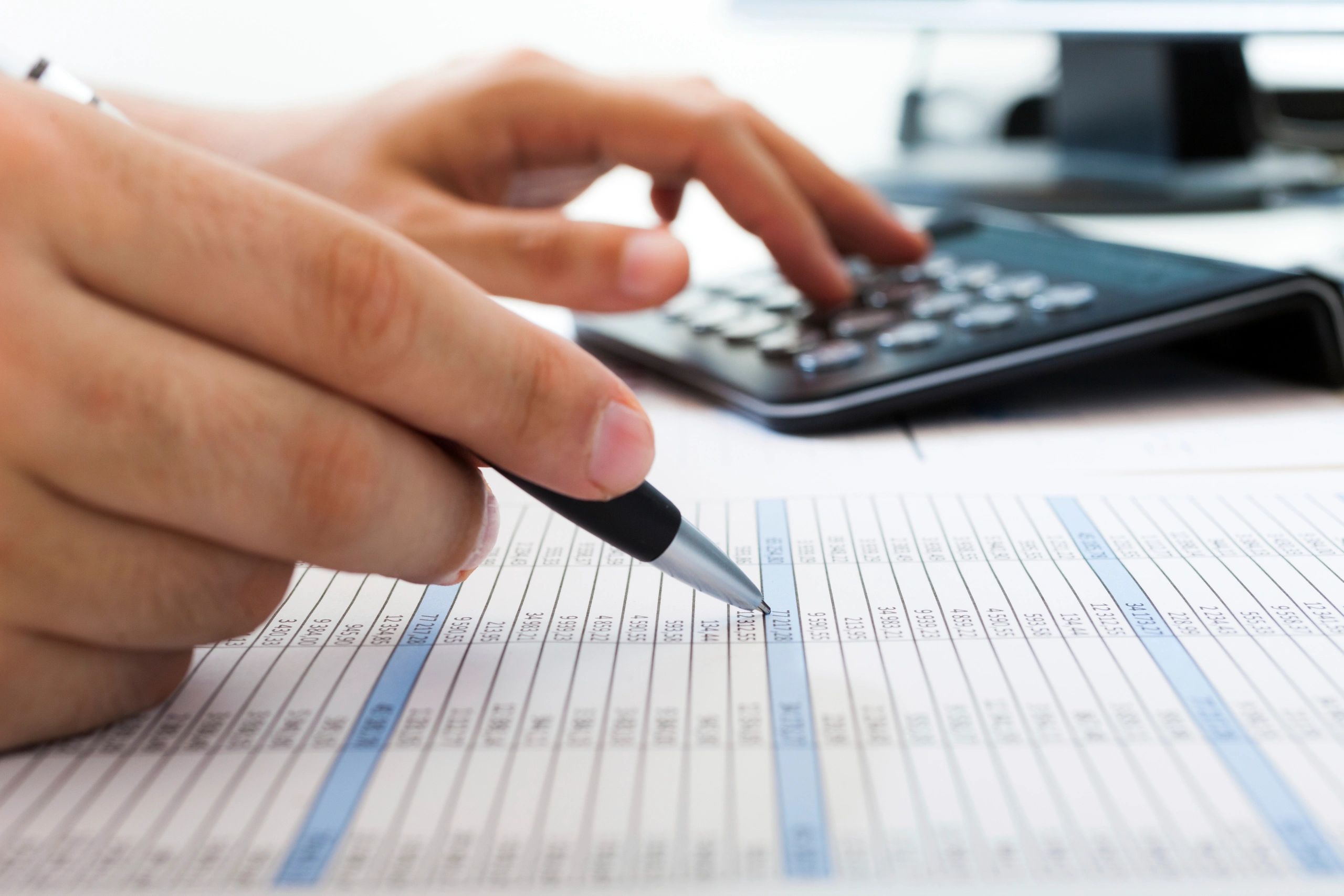 Person writing on a financial spreadsheet with a pen